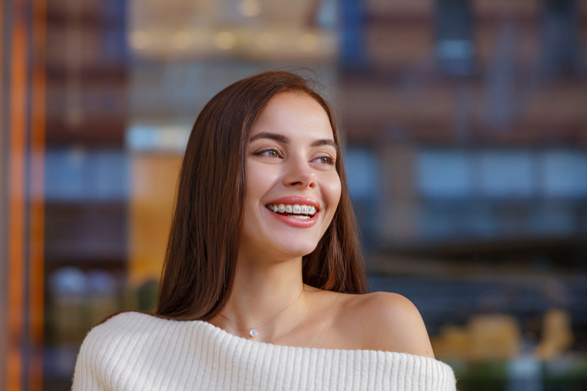 Emotional portrait of a beautiful happy smiling young woman with braces. Attractive girl with bracket system posing in city outdoor. Brace, bracket, dental care, malocclusion, orthodontic health concept, blurred.